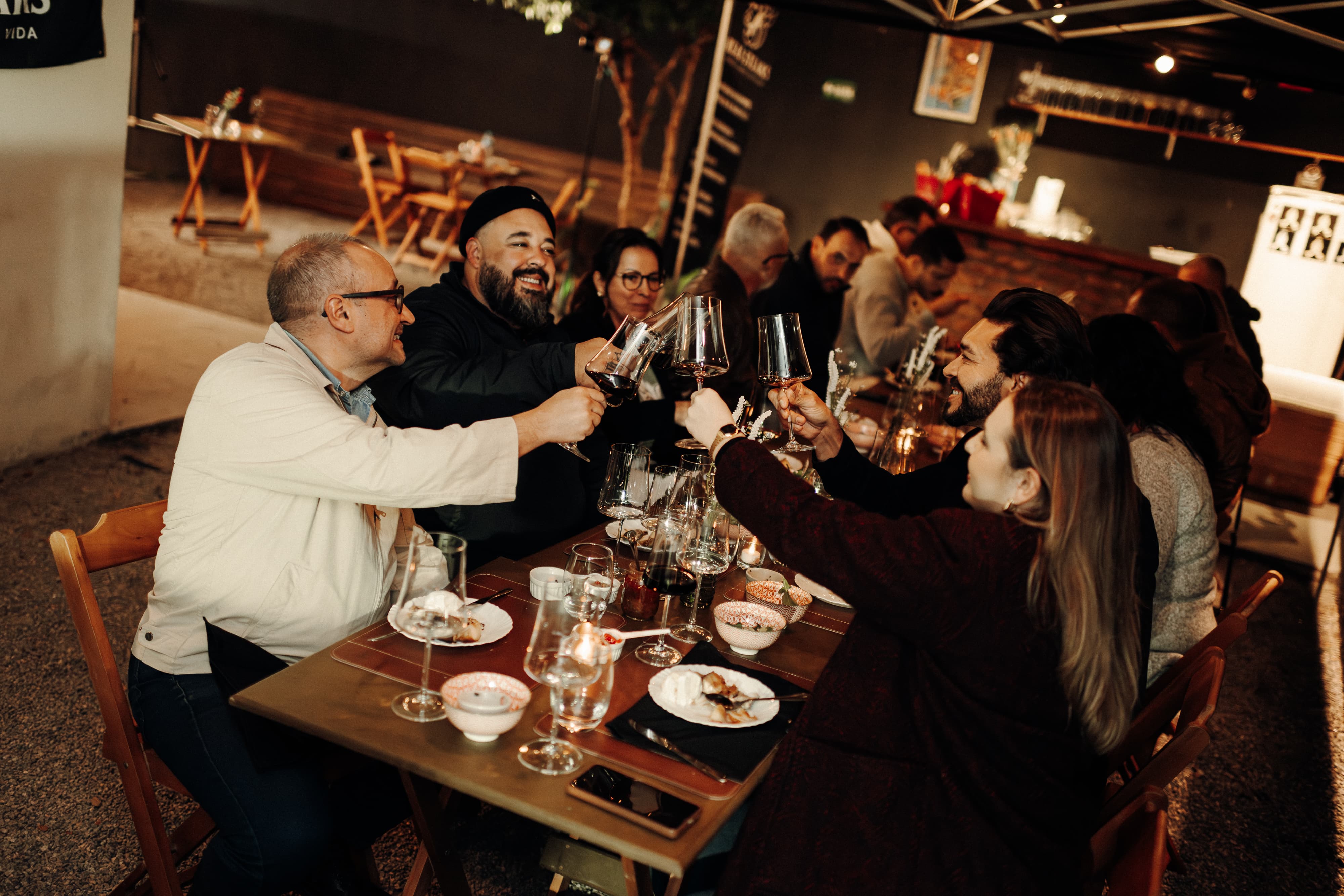 Grupo de amigos brindando com vinho tinto em uma mesa no Quintal Real à noite